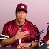 Dwayne Johnson i młoda dziewczyna w strojach drużyny sportowej, z rękami na sercu, przygotowują się do wygłoszenia przemówienia. Plan gry jest gotowy.