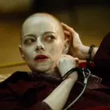 Emma Stone w kajdankach, z ogoloną głową i makijażem, jak w filmach Yorgosa Lanthimosa.