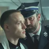 Młody ksiądz i policjant w mundurze, w tle widać innych mężczyzn. Scena z filmu "Boże Ciało", którego reżyserem jest Jan Komasa.