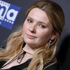 Abigail Breslin, znana z wielu filmów, z niebieskimi oczami i blond włosami, pozuje z uśmiechem.
