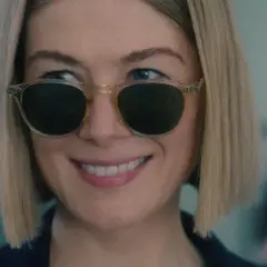 Uśmiechnięta Rosamund Pike w okularach przeciwsłonecznych, przypominająca scenę z jej filmów i seriali.