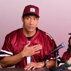 Dwayne Johnson i młoda dziewczyna w strojach drużyny sportowej, z rękami na sercu, przygotowują się do wygłoszenia przemówienia. Plan gry jest gotowy.