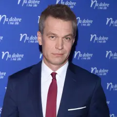 Michał Żebrowski w garniturze, znany z wielu filmów, pozuje na tle niebieskiej ścianki z napisem "Na dobre i na złe".