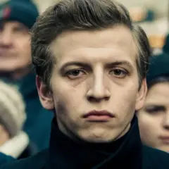 Młody mężczyzna na pierwszym planie, otoczony tłumem. Jego wyraz twarzy sugeruje głębokie przemyślenia, jakby przygotowywał się do roli w jednym z filmów Macieja Musiałowskiego.