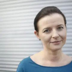 Uśmiechnięta Jowita Budnik, aktorka znana z wielu polskich filmów, na tle szarej, falistej ściany.