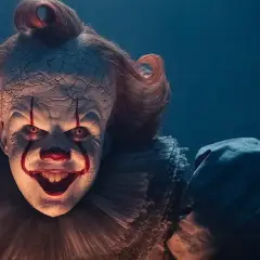Przerażający klaun Pennywise z czerwonymi włosami i makijażem, z uśmiechem zapowiadającym kłopoty.