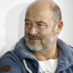 Siwy brodacz, jakby z jednego z filmów Jana Jakuba Kolskiego, w niebieskiej bluzie z kapturem.