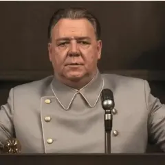 Russell Crowe w szarym mundurze, z mikrofonem przed sobą. Scena z jednego z jego filmów.