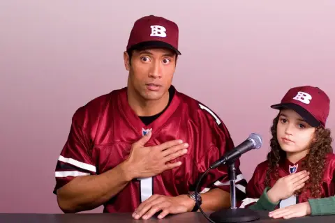 Dwayne Johnson i młoda dziewczyna w strojach drużyny sportowej, z rękami na sercu, przygotowują się do wygłoszenia przemówienia. Plan gry jest gotowy.