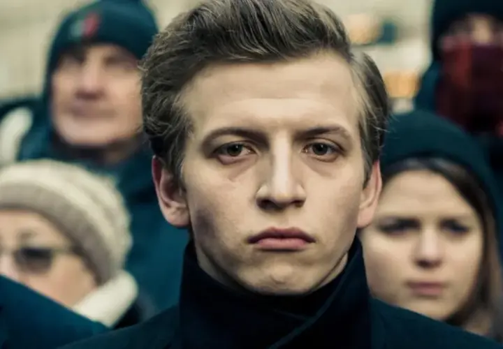Młody mężczyzna na pierwszym planie, otoczony tłumem. Jego wyraz twarzy sugeruje głębokie przemyślenia, jakby przygotowywał się do roli w jednym z filmów Macieja Musiałowskiego.