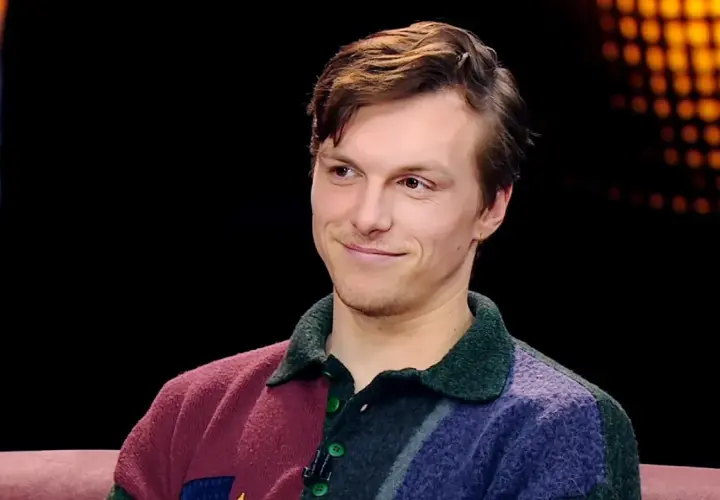 Uśmiechnięty Tomasz Włosok, aktor znany z wielu filmów, w kolorowym swetrze.