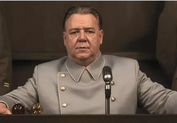 Russell Crowe w szarym mundurze, z mikrofonem przed sobą. Scena z jednego z jego filmów.