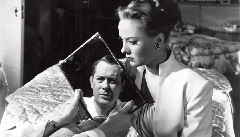 Kobieta trzyma lustro, w którym odbija się mężczyzna z blizną na twarzy. Klimat typowy dla **film noir**.