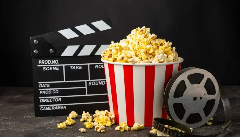 Klapka filmowa, kubełek popcornu i rolka taśmy filmowej na ciemnym tle.
