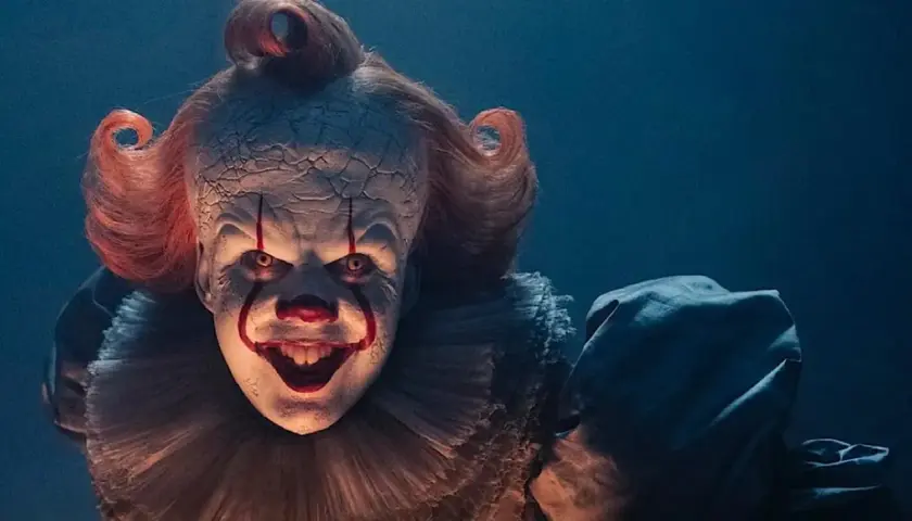 Przerażający klaun Pennywise z czerwonymi włosami i makijażem, z uśmiechem zapowiadającym kłopoty.