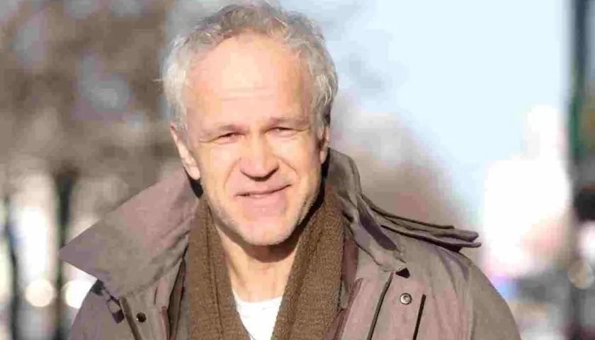 Uśmiechnięty Radosław Pazura w brązowym szaliku i kurtce, przypomina o swoich niezapomnianych rolach w polskich filmach.
