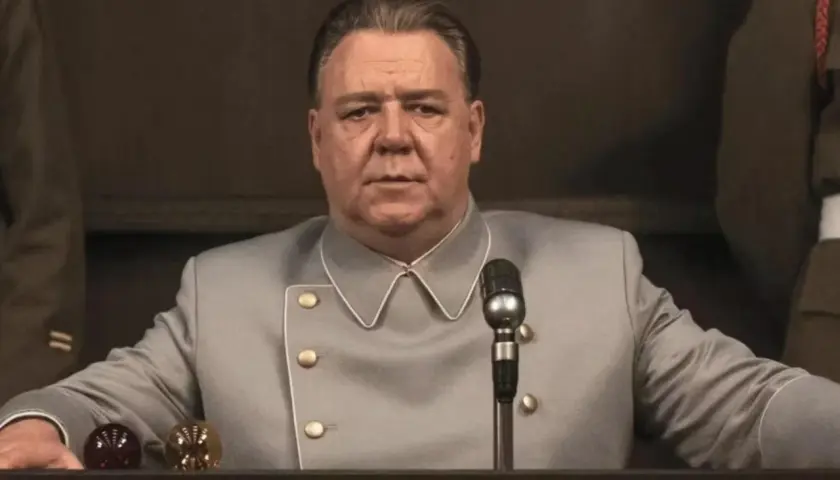 Russell Crowe w szarym mundurze, z mikrofonem przed sobą. Scena z jednego z jego filmów.