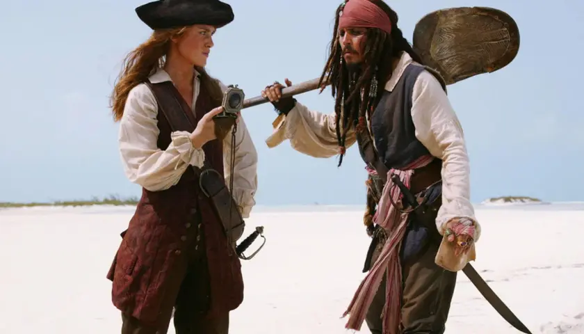 Elizabeth Swann i Kapitan Jack Sparrow, bohaterowie filmów "Piraci z Karaibów", stoją na plaży, rozmawiając.