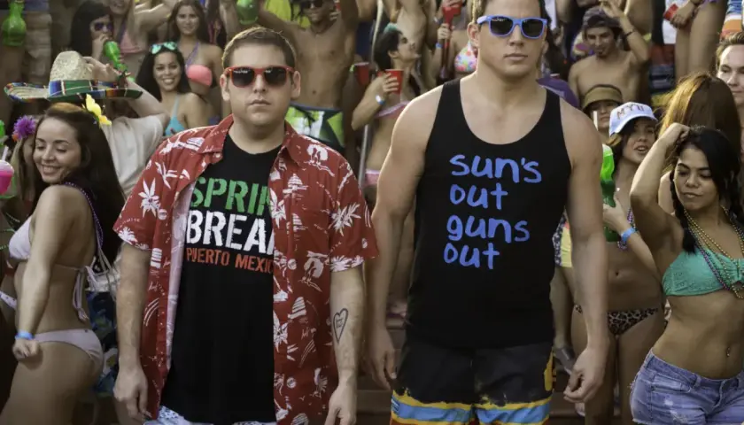 Dwóch facetów w okularach przeciwsłonecznych, jeden w koszulce "Spring Break Puerto Mexico", drugi w "Sun's out guns out", na imprezie w stylu jump street 23.