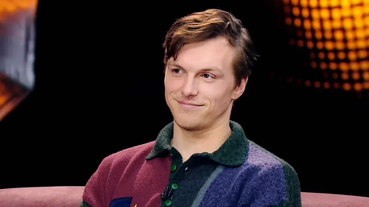 Uśmiechnięty Tomasz Włosok, aktor znany z wielu filmów, w kolorowym swetrze.