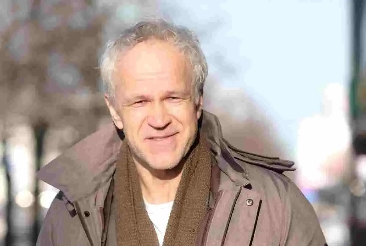 Uśmiechnięty Radosław Pazura w brązowym szaliku i kurtce, przypomina o swoich niezapomnianych rolach w polskich filmach.