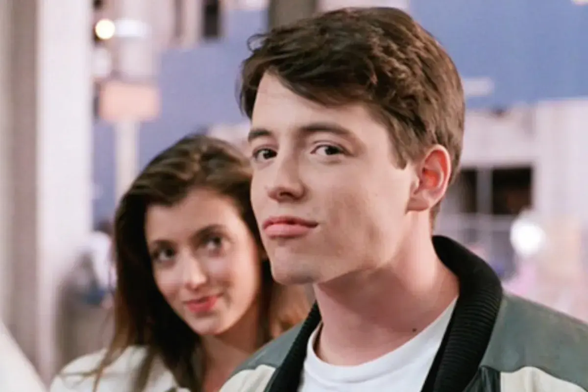 Matthew Broderick w jednym z kultowych matthew broderick filmów, uśmiecha się do kamery, podczas gdy za nim widać kobietę.