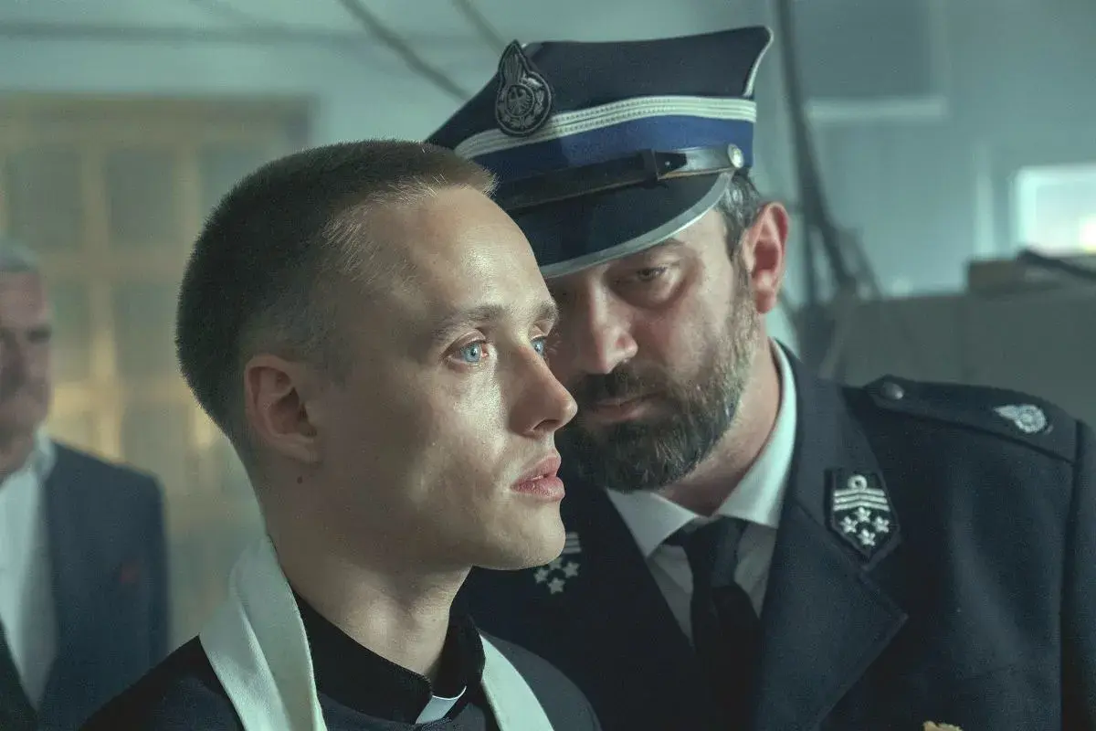 Młody ksiądz i policjant w mundurze, w tle widać innych mężczyzn. Scena z filmu "Boże Ciało", którego reżyserem jest Jan Komasa.