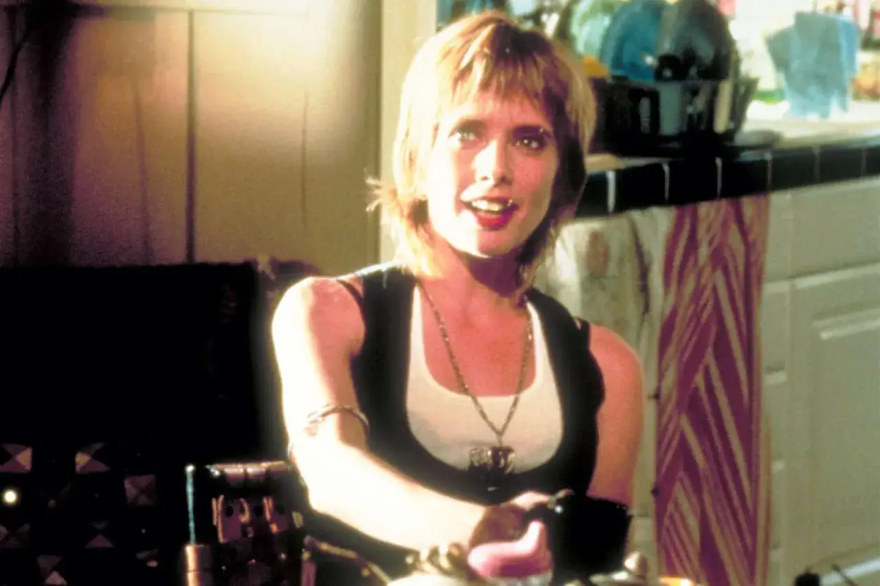Rosanna Arquette w filmach, z charakterystyczną fryzurą i biżuterią, uśmiecha się do kamery.