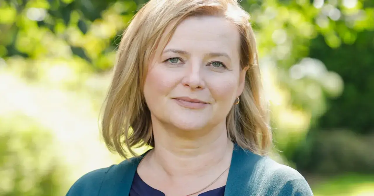 Uśmiechnięta Jowita Budnik, aktorka znana z wielu filmów, na tle zieleni.