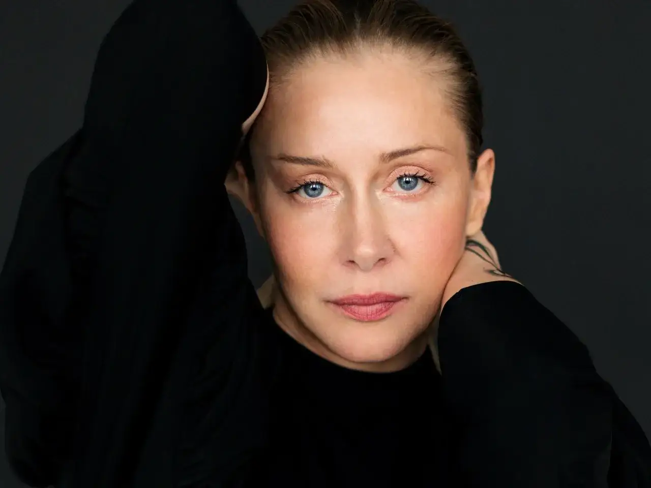 Katarzyna Warnke w czerni, z rękami przy głowie. Jej niebieskie oczy patrzą prosto w obiektyw, jakby zapraszała do świata swoich filmów.