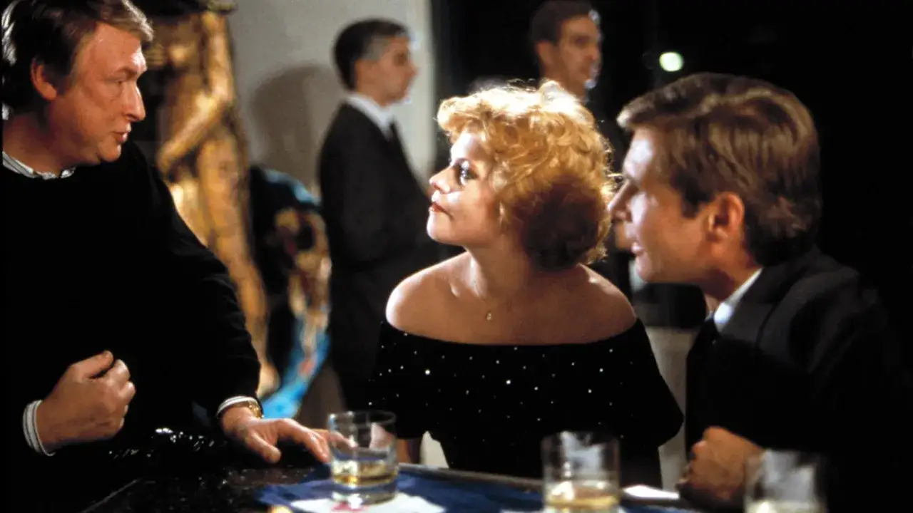 Melanie Griffith w czarnej, błyszczącej sukni, rozmawia z mężczyznami przy barze. Scena z jednego z jej filmów.