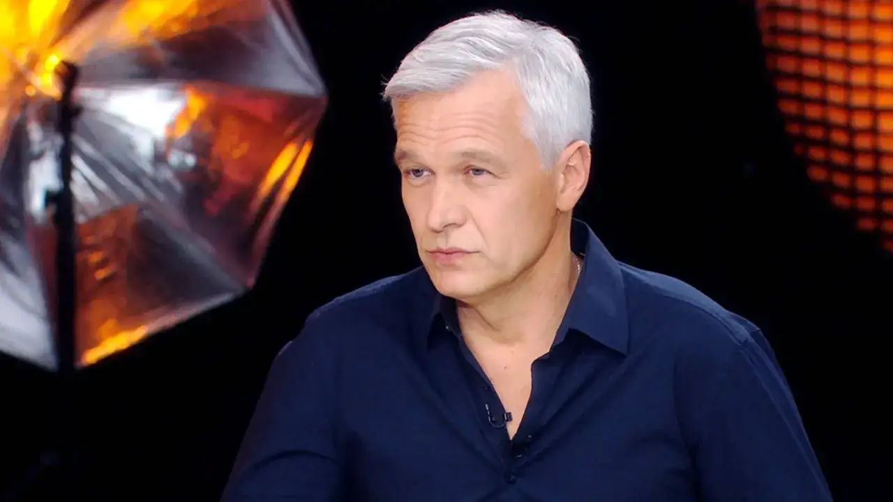 Michał Żebrowski, znany z wielu filmów, w ciemnej koszuli, z siwymi włosami, na tle studyjnym.