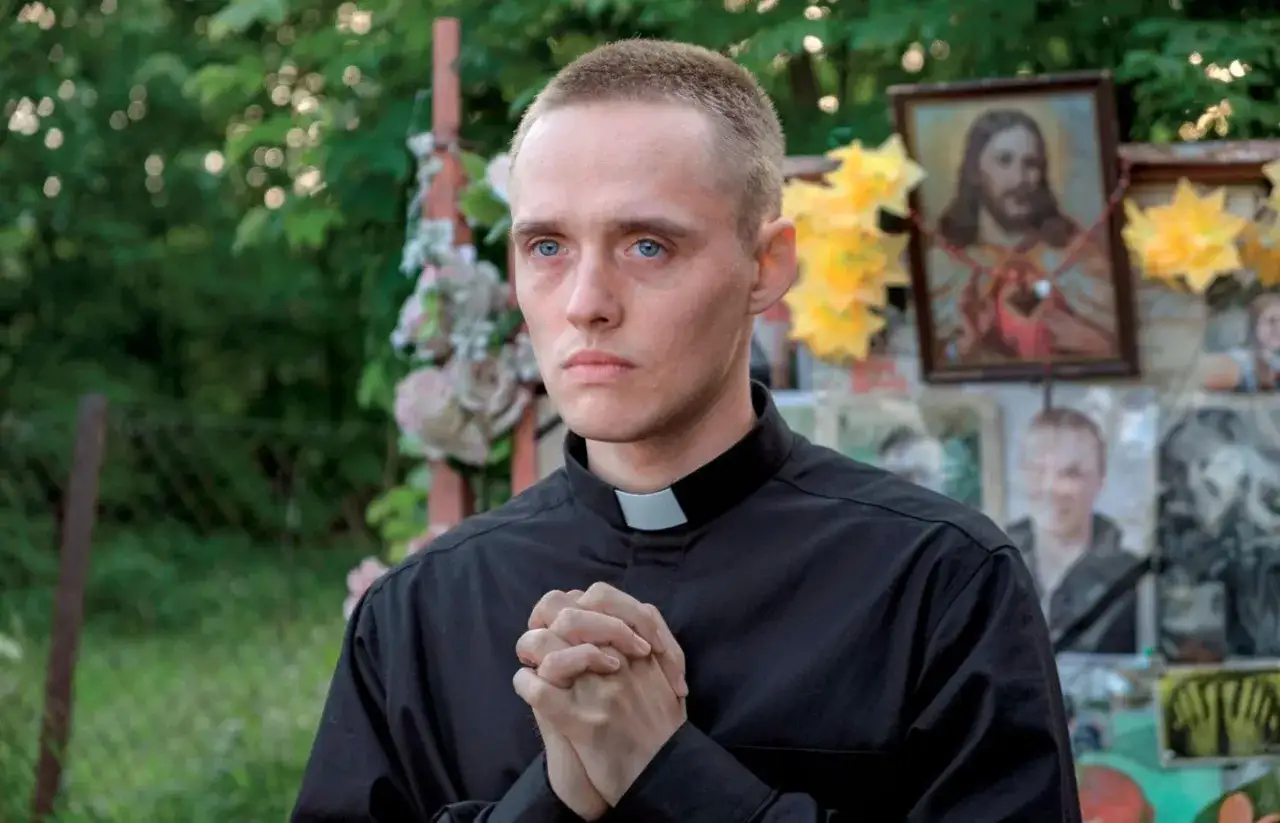 Młody mężczyzna w sutannie, z dłońmi złożonymi do modlitwy, przypomina postać reżysera filmu 